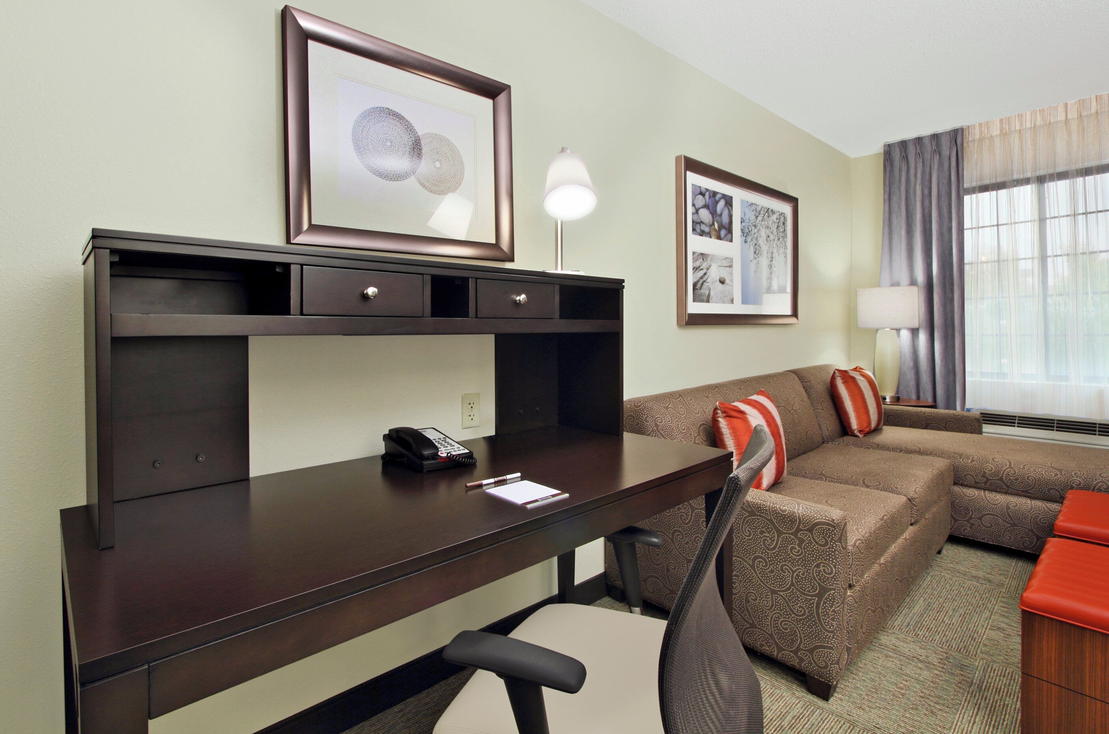 A hotel room with a desk, chair, and a sofa with decorative pillows.