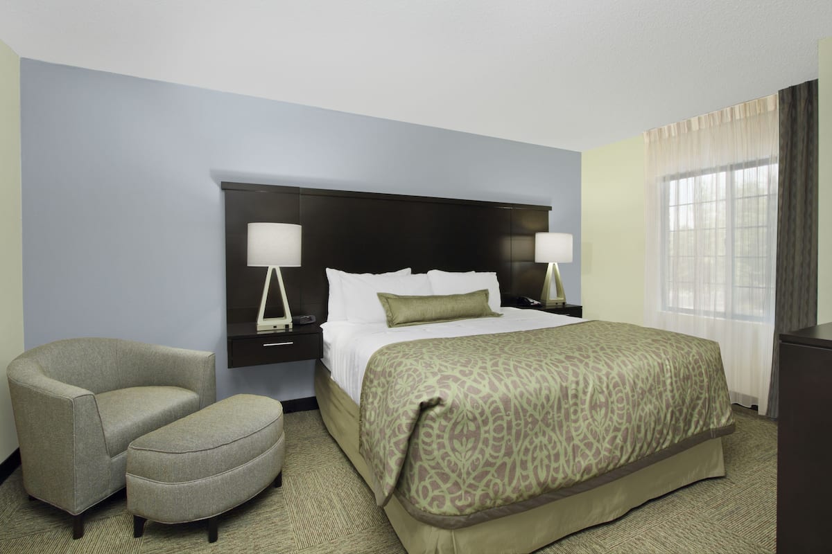 A hotel room with a large bed, two bedside tables with lamps, a chair, and a desk.