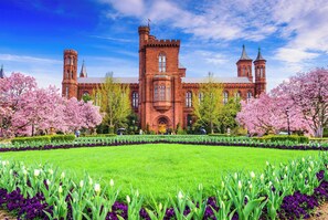 A historic building with a central tower and two smaller towers, surrounded by a well-manicured garden with flowering trees. - Staybridge Suites Tysons - McLean by IHG (McLean)