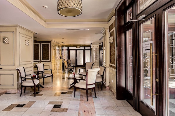 Vestíbulo de hotel con piso de mármol, varias mesas de comedor y sillas.
