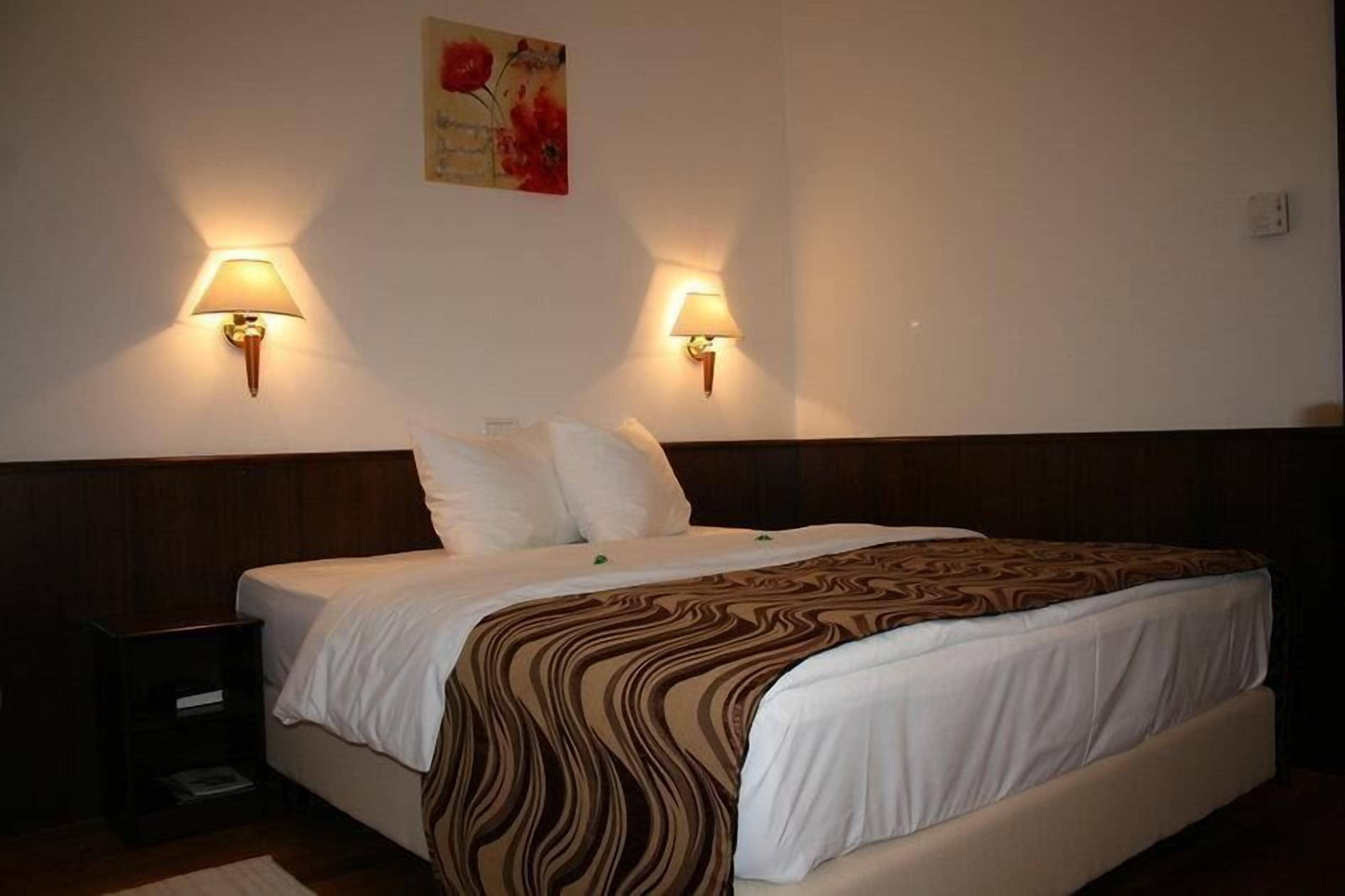Una habitación de hotel con una cama grande, dos lámparas de pared y un cuadro en la pared.