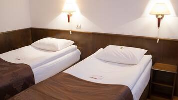 Habitación de hotel con dos camas individuales, cada una con almohada y manta. Hay lámparas de pared a ambos lados de las camas.