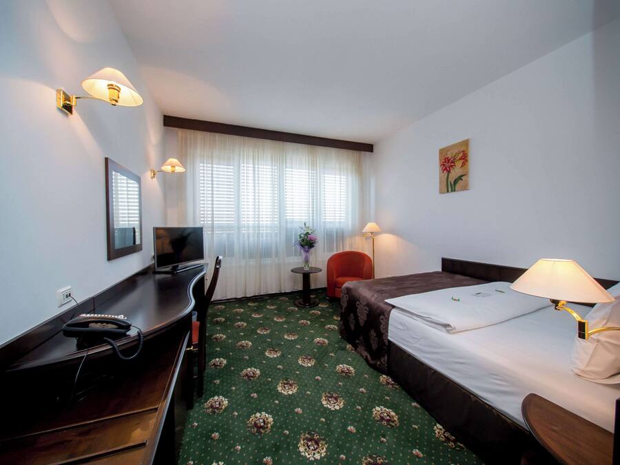 Habitación de hotel con escritorio, dos camas, una silla, televisor y ventana con cortinas.