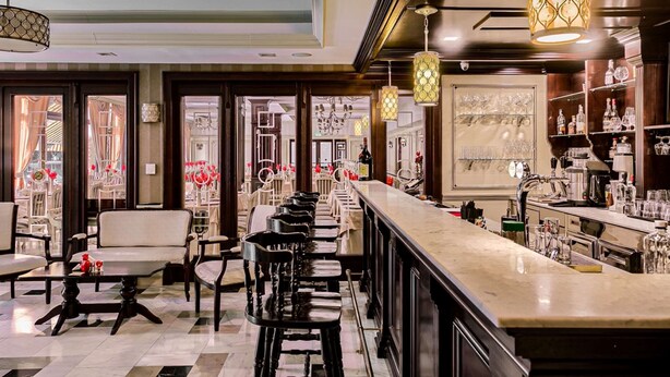 A bar area with a long counter, bar stools, and a chandelier. - Best Western Central Hotel (Arad)
