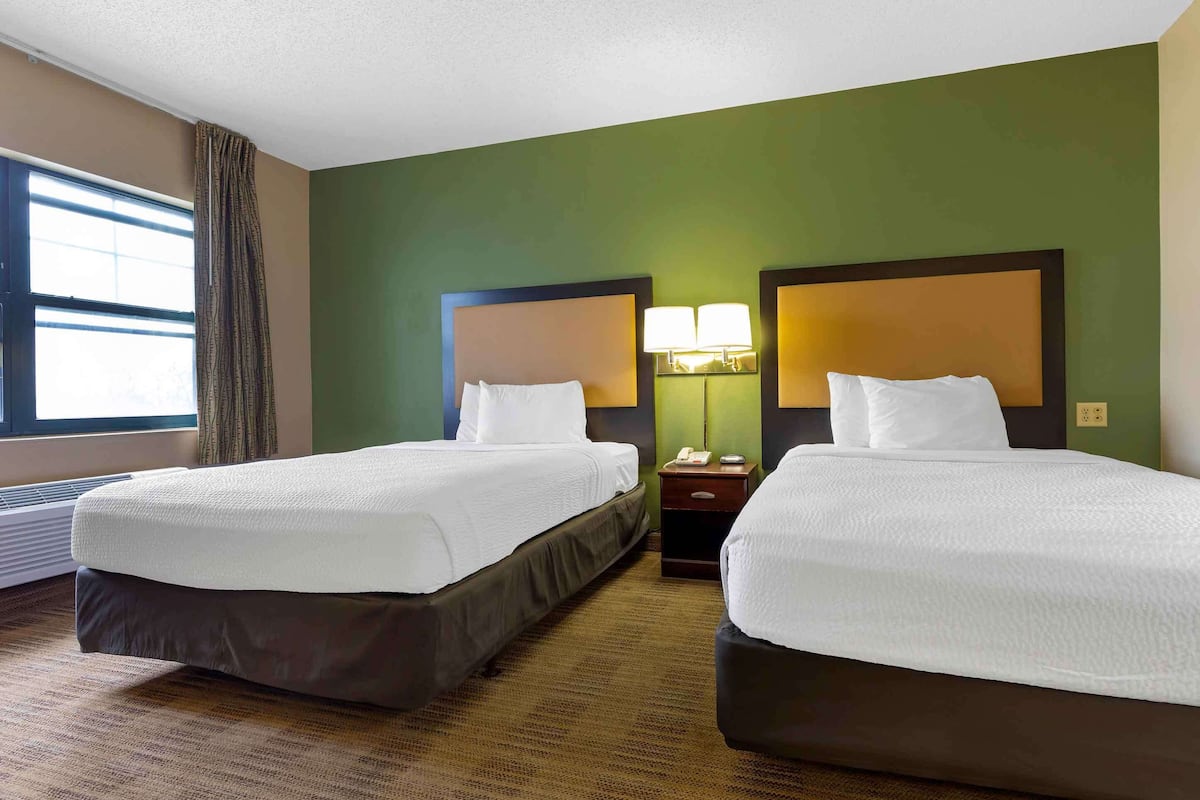 A hotel room with two beds, green walls, and a window with curtains.