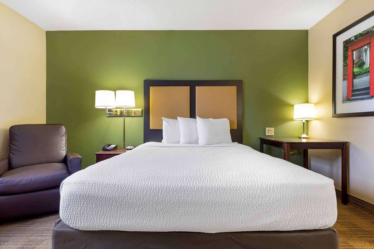 A hotel room with a large bed, two bedside lamps, a chair, and a nightstand.