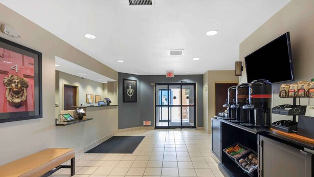 Un hall con mostrador de recepción, un banco, estación de café y un televisor en la pared.