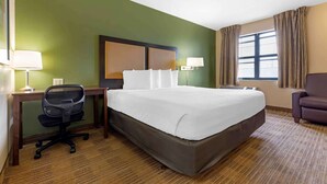 Una habitación de hotel con una cama grande, un escritorio con silla, una lámpara y una ventana con cortinas.