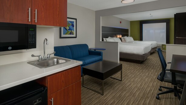 A compact hotel room with a kitchenette, a blue sofa, a single bed, and a desk with a chair. - Holiday Inn Express & Suites Lawrence by IHG (Lawrence)