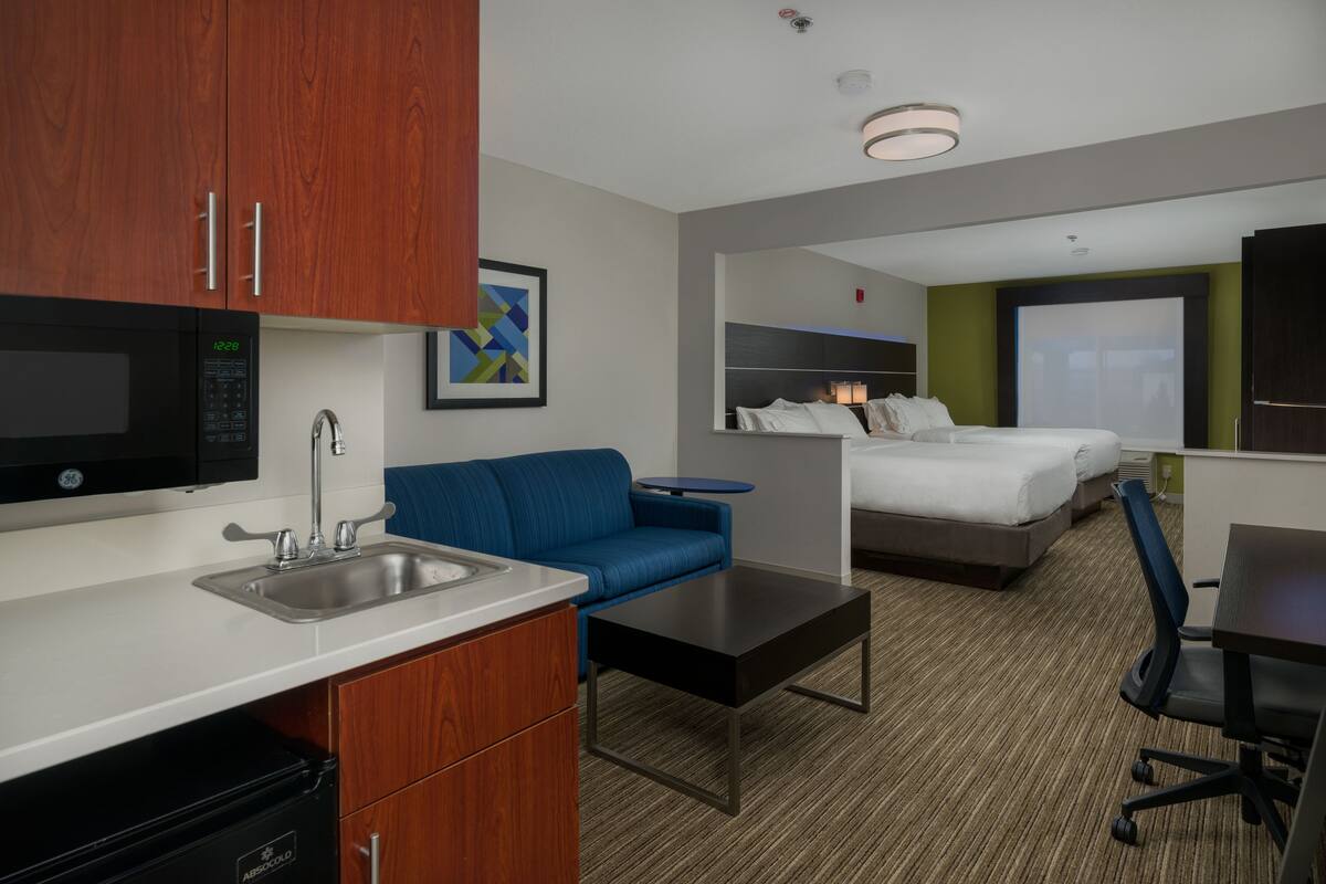Una habitación de hotel compacta con kitchenette, un sofá azul, una cama individual y un escritorio con silla.