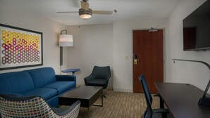 A modern room with a blue sofa, a patterned armchair, a small table, a ceiling fan, and a TV mounted on the wall. - Holiday Inn Express & Suites Lawrence by IHG (Lawrence)