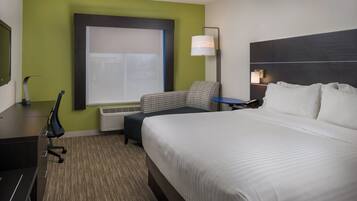 A hotel room with a bed, a desk, a chair, a lamp, and a window.