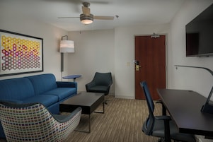 Una sala moderna con un sofá azul, un sillón estampado, una mesita, un escritorio y un ventilador de techo.