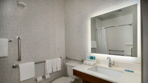 A bathroom with a toilet, sink, and mirror. There are handrails, a fire alarm, and a towel rack. - Holiday Inn Express & Suites Lawrence by IHG (Lawrence)