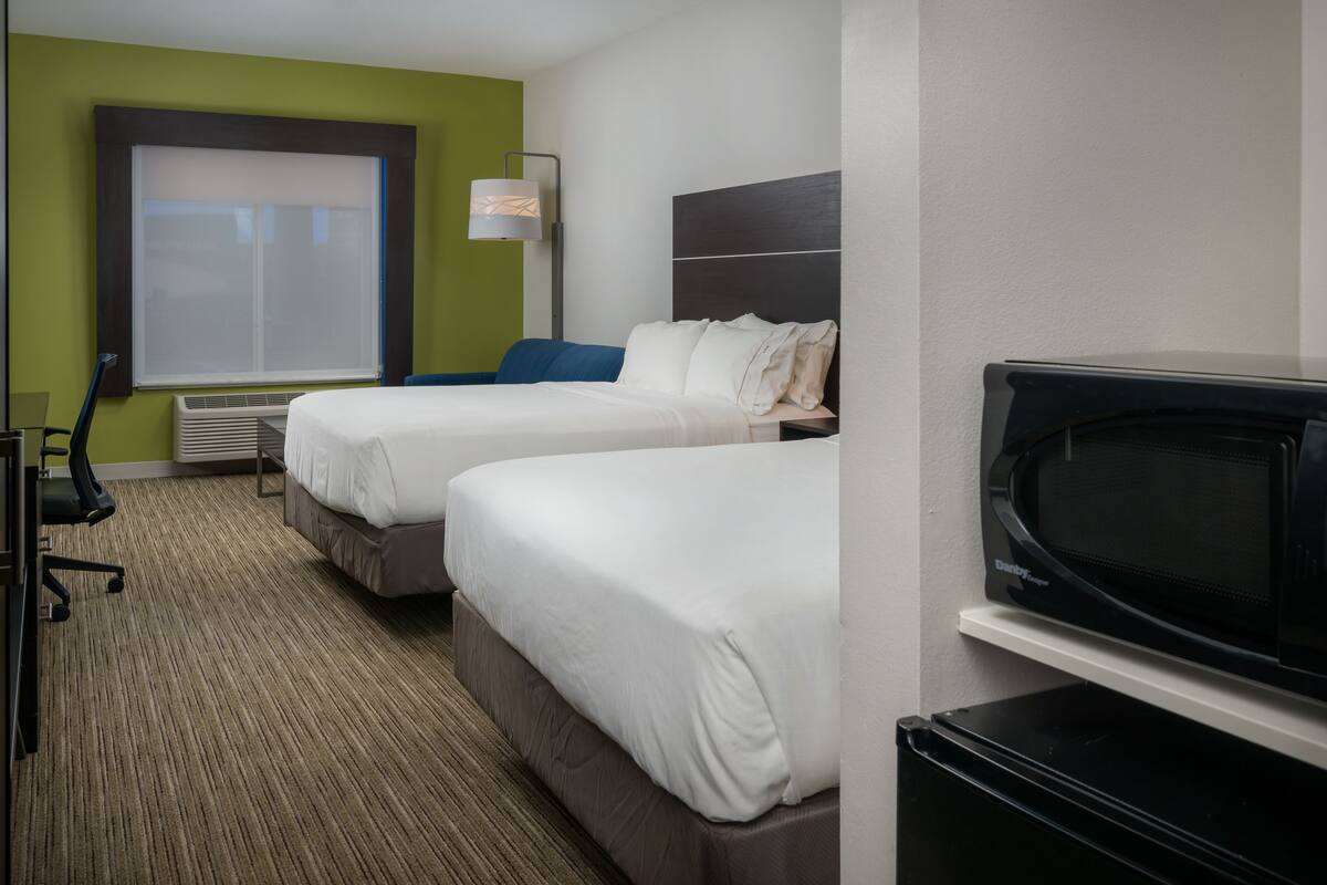 Habitación de hotel con dos camas, un escritorio, una silla, un televisor y una ventana con persianas.