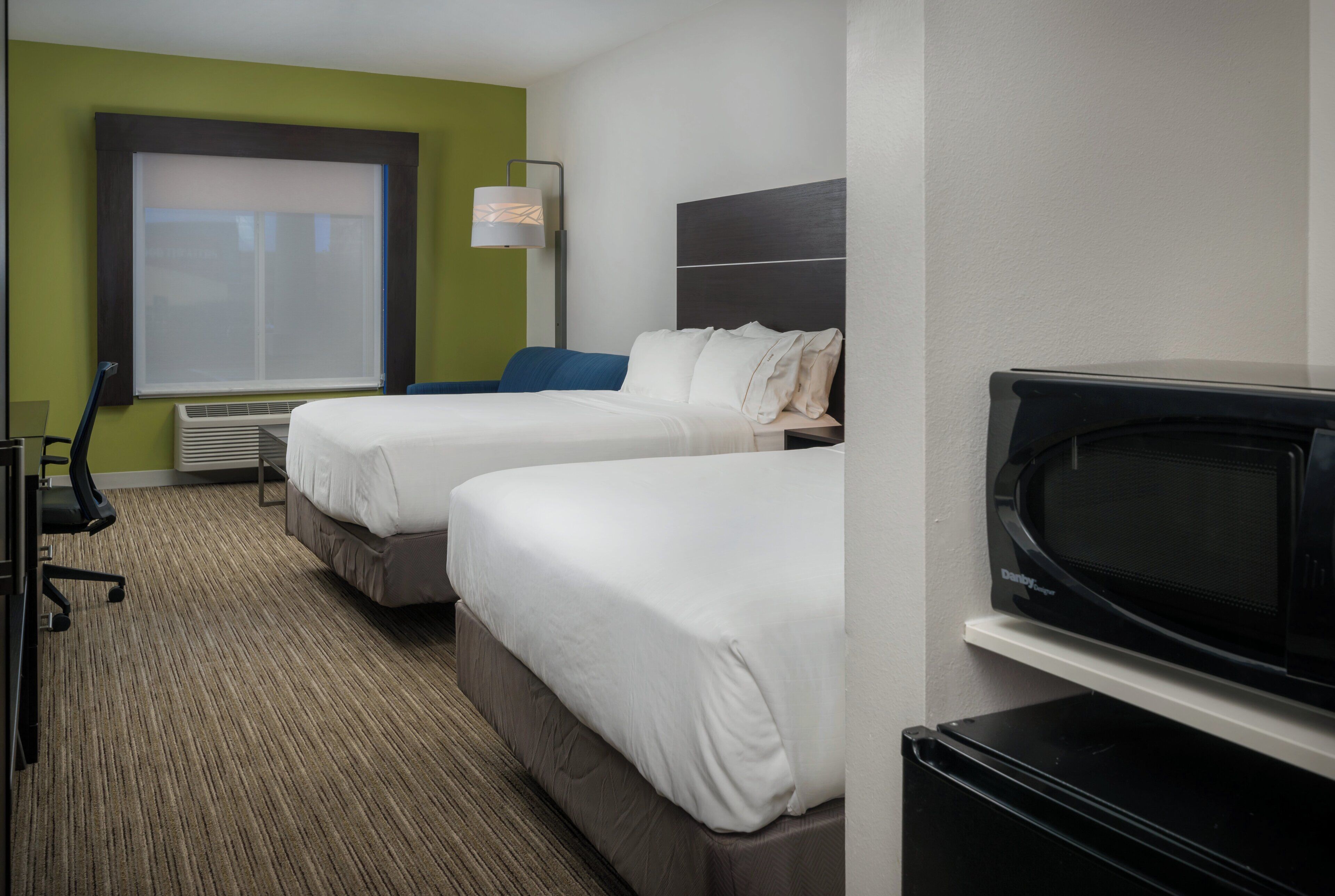 A hotel room with two beds, a desk, a chair, a television, and a window with blinds.