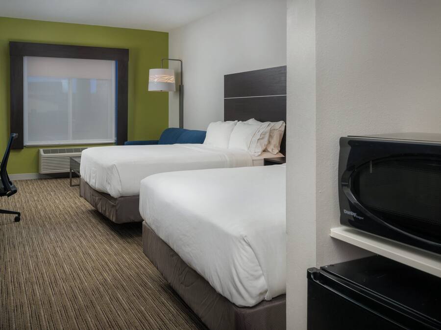 A hotel room with two beds, a desk, a chair, a television, and a window with blinds.