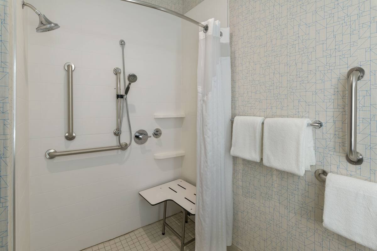 Un baño con ducha, barras de apoyo, un asiento y un perchero para toallas.