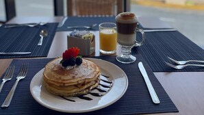 A breakfast setting with pancakes, a glass of orange juice, and a coffee drink, with a view of the beach and palm trees in the background. - DoubleTree by Hilton Hotel Veracruz (Veracruz)