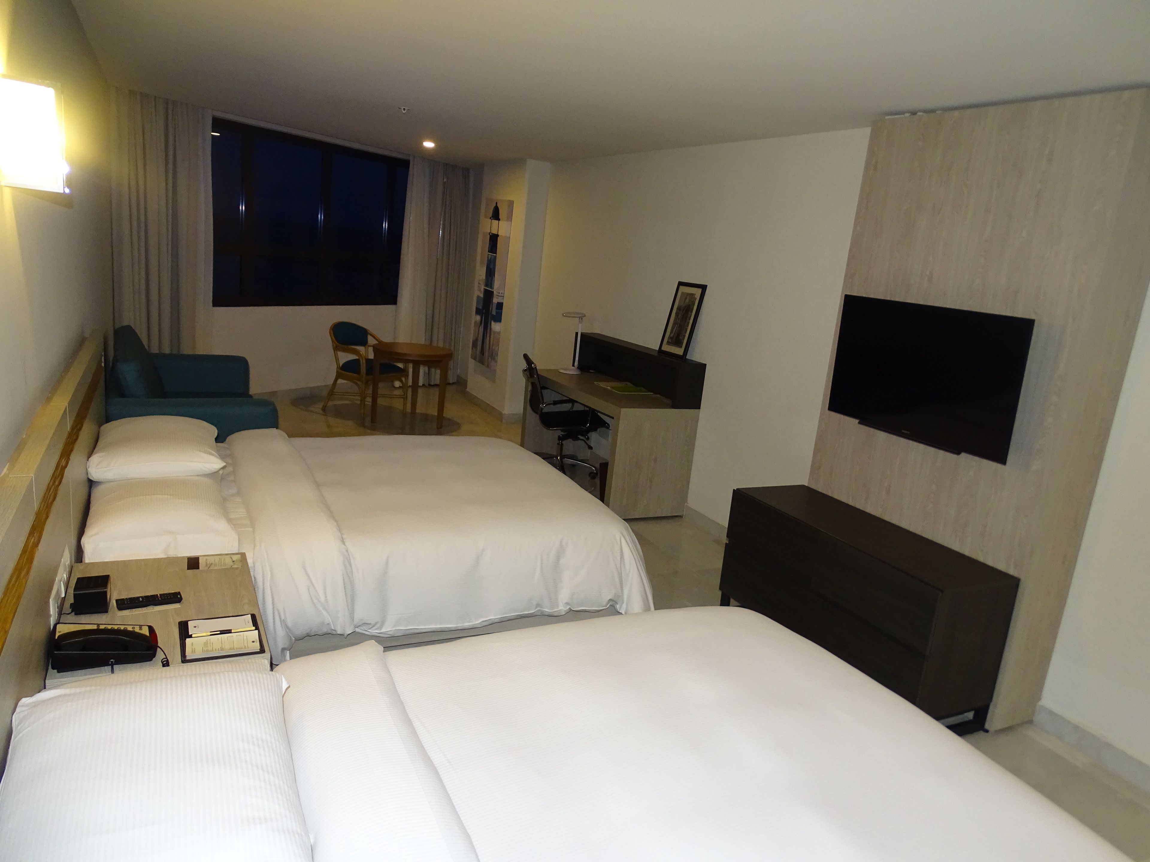 A hotel room with two beds, a desk, a chair, a TV, and a large window.