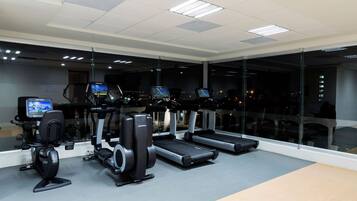 A gym with treadmills, elliptical machines, and a stationary bike, featuring large windows and a city view.