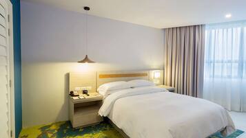 A hotel room with a bed, bedside tables, a lamp, and a window with curtains.