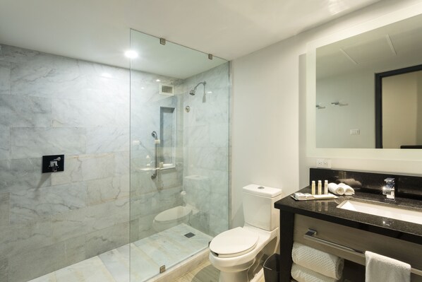 Un baño moderno con ducha de vidrio, inodoro blanco y tocador negro con espejo.