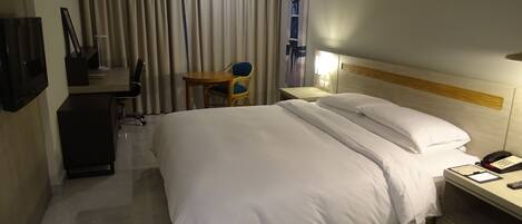 A hotel room with a large bed, a desk with a chair, a TV, and a lamp.