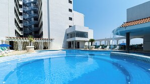 A swimming pool with clear blue water, surrounded by lounge chairs and umbrellas, and adjacent to a modern building with balconies. - DoubleTree by Hilton Hotel Veracruz (Veracruz)