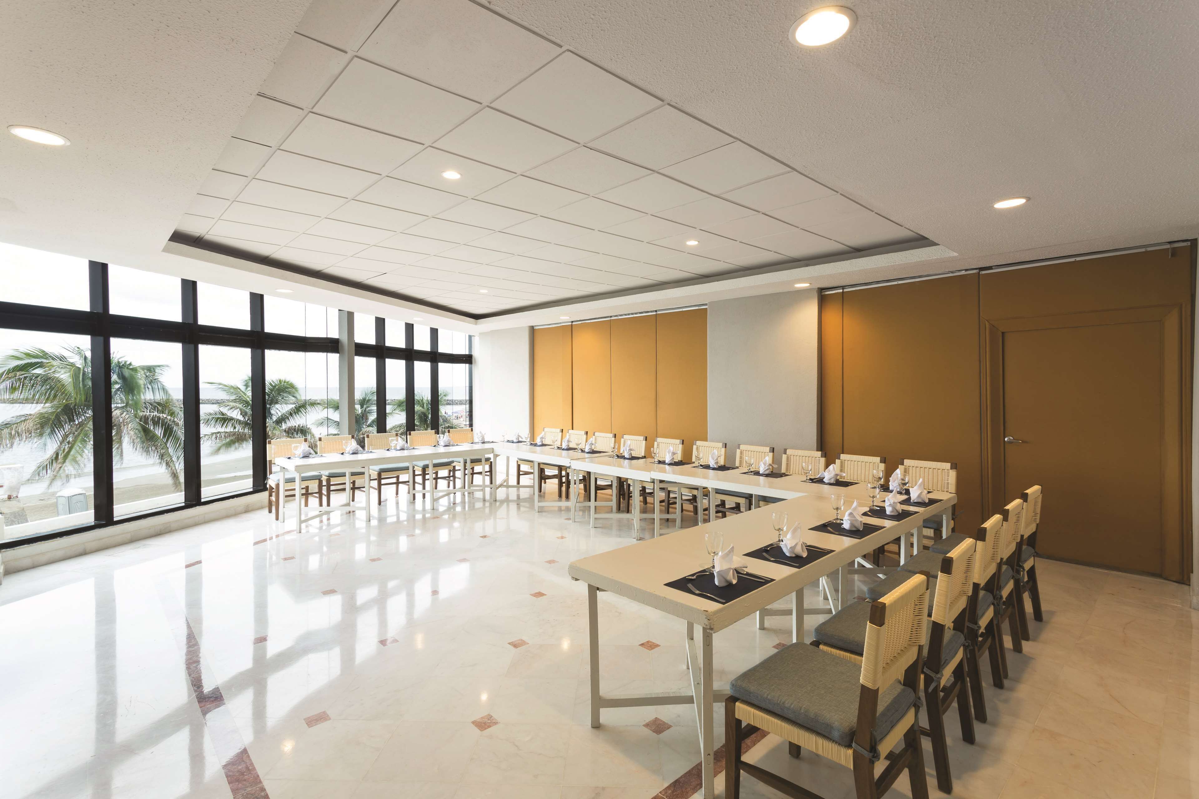 A conference room with long tables, chairs, and a large window with a view of palm trees.