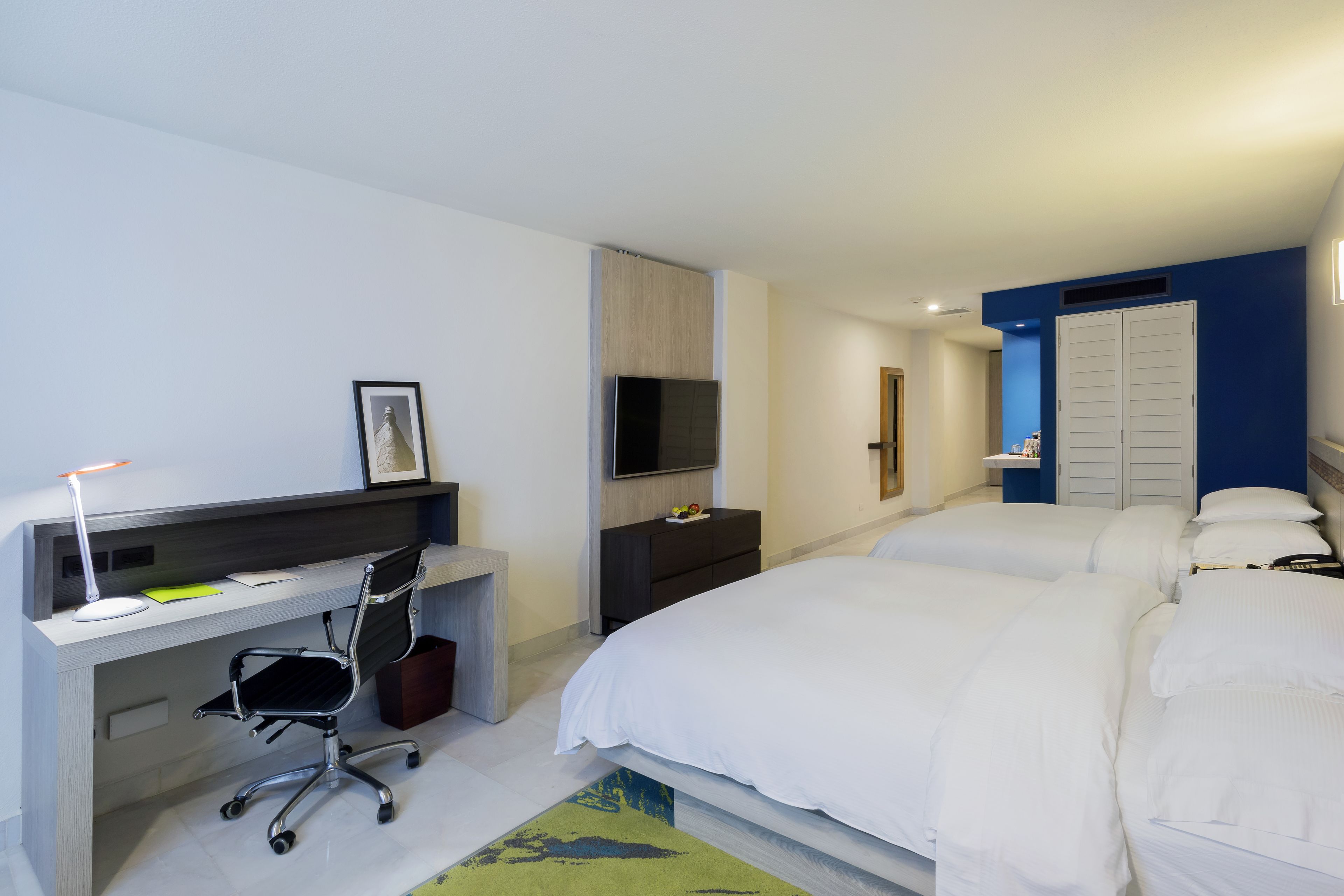 A hotel room with a desk, chair, two beds, a TV, and a wardrobe.