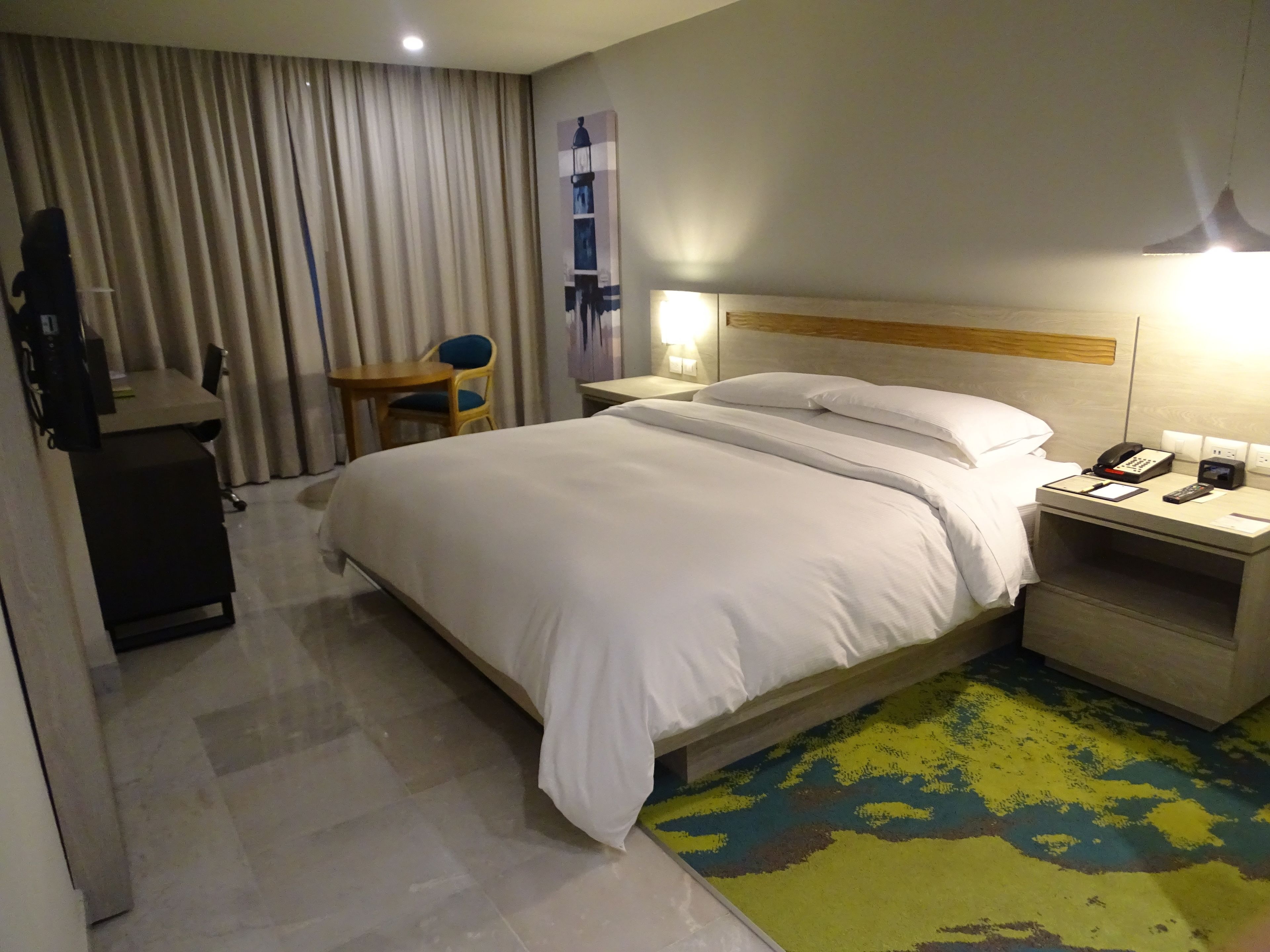 Habitación de hotel con una cama grande, una mesita de noche con teléfono y lámpara, un escritorio con silla y una cortina.