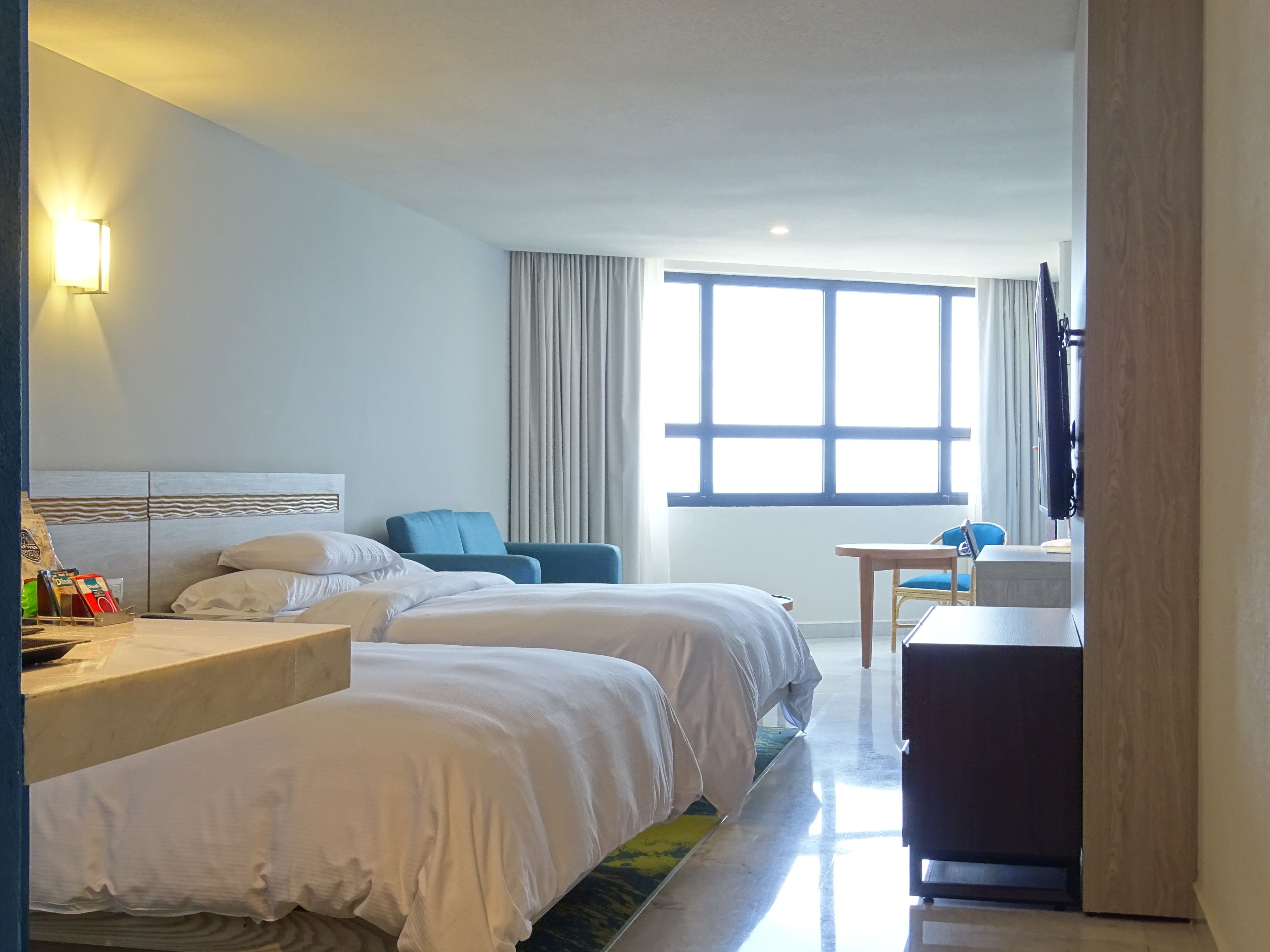 Een hotelkamer met twee bedden, een bureau, een stoel, een televisie en een groot raam.