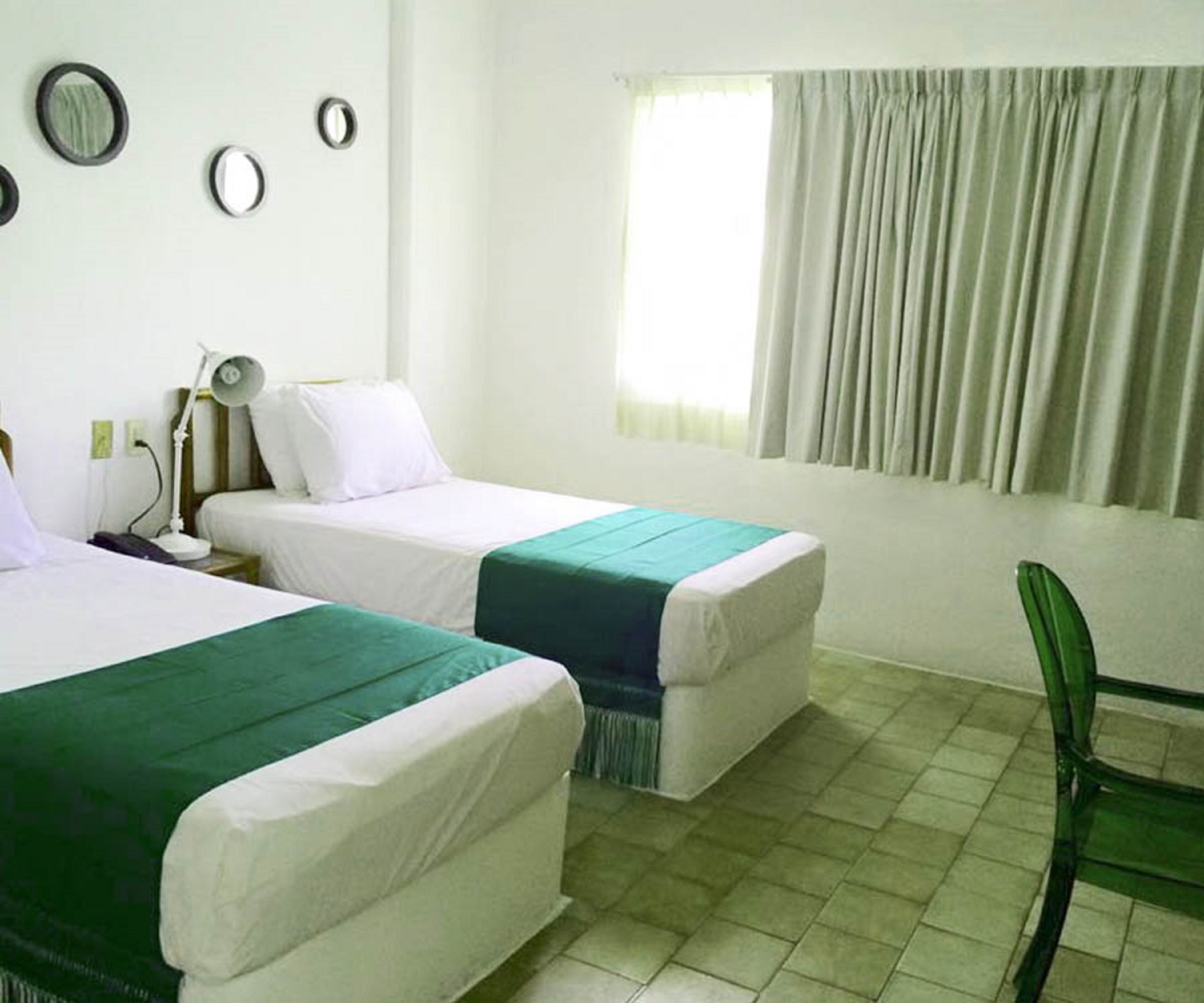 Habitación de hotel con dos camas, un escritorio, una silla y un ventanal con cortinas.