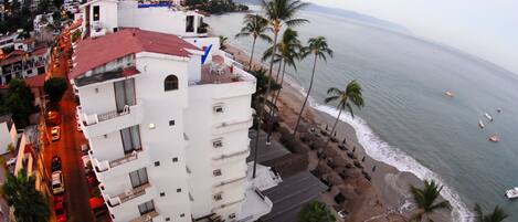 Un hôtel situé sur la côte, avec un toit rouge, des murs blancs et un balcon donnant sur la plage.