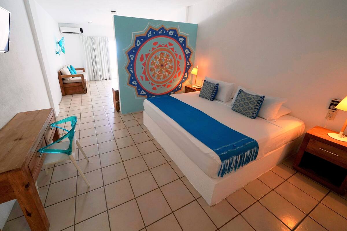 Ein Hotelzimmer mit Bett, Nachttisch, Lampe, Stuhl, Tisch und einer Wanddekoration.