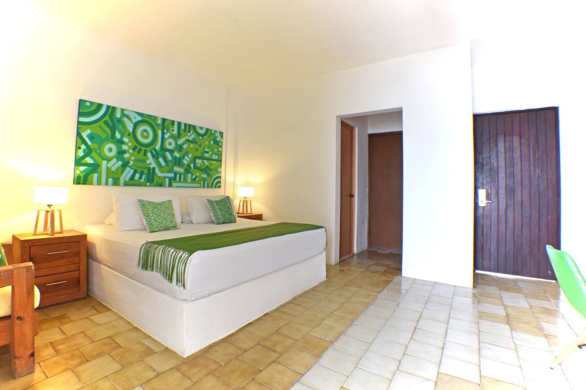 Ein Schlafzimmer mit einem Bett, Nachttischen, einem abstrakten grünen Gemälde und einer Holztür.
