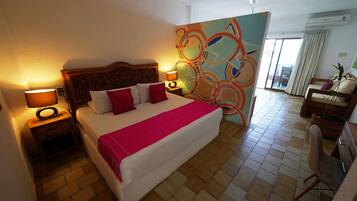 Habitación de hotel con una cama grande, dos mesitas de noche con lámparas, un ventilador de techo, una pared con un diseño abstracto colorido y vistas al exterior a través de una puerta corredera.