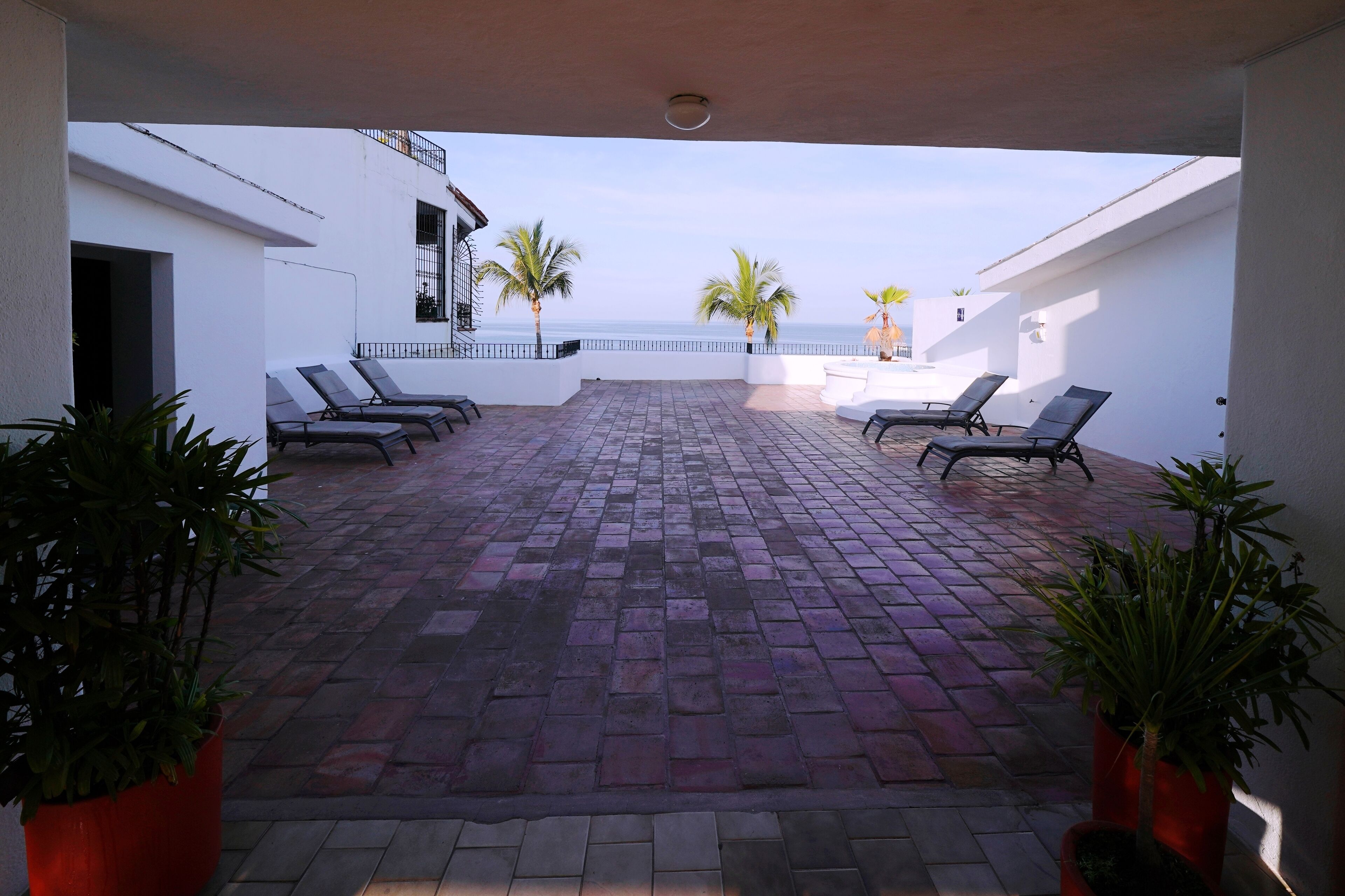 An outdoor patio with a tiled floor, several lounge chairs, and potted plants.