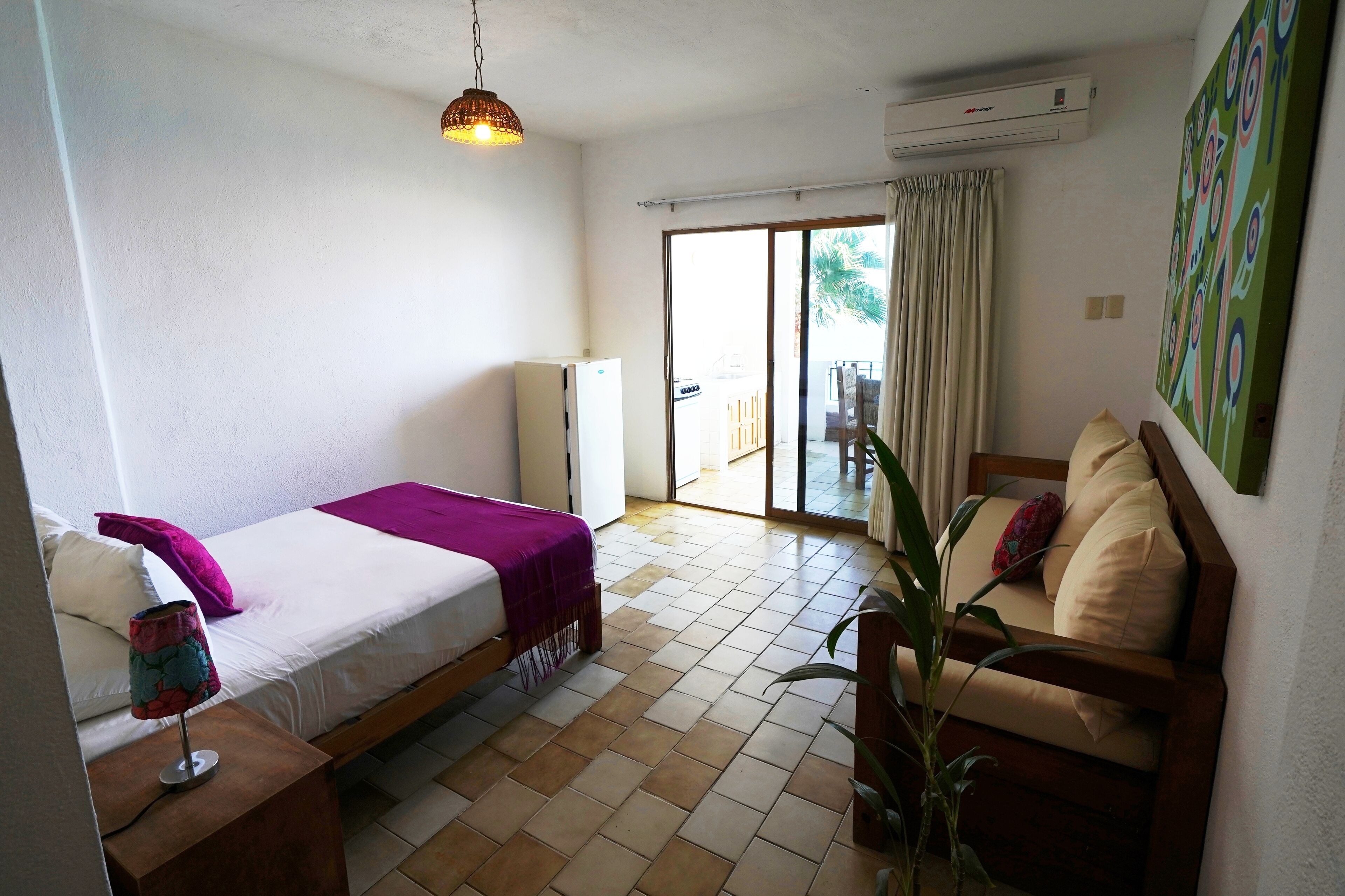Una habitación con una cama, un sofá, una mesita y una planta en maceta.