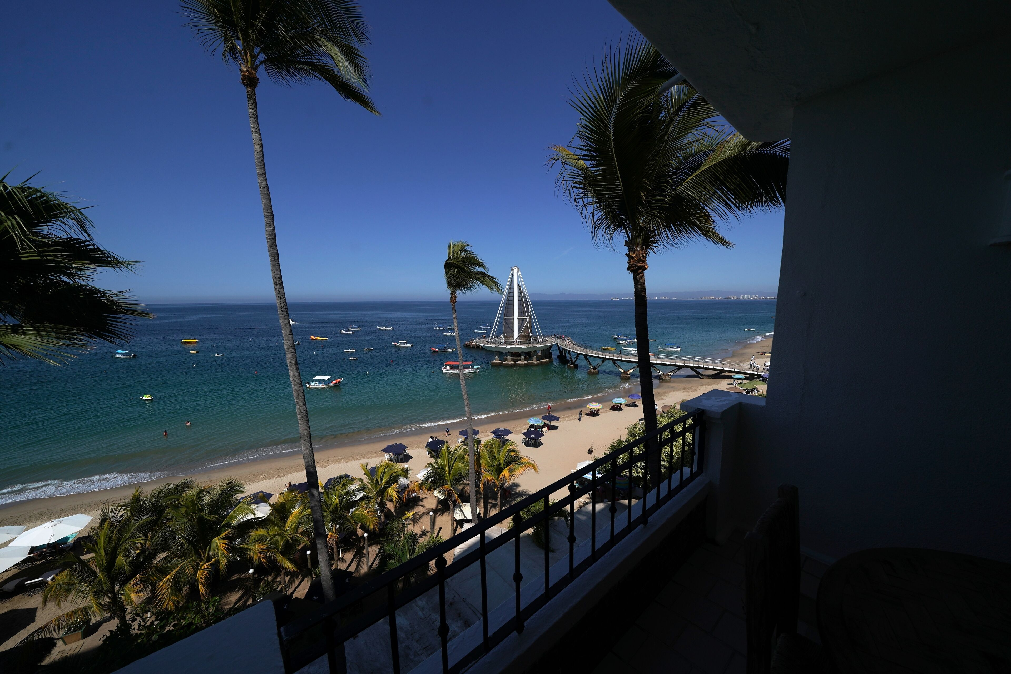A beach view with palm trees, a pier, and boats.