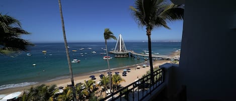 A beach view with palm trees, a pier, and boats.