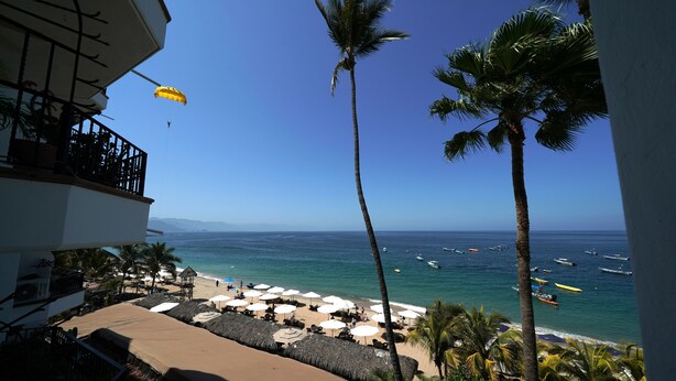 A beach view with umbrellas, palm trees, and boats on the water. - Emperador Vallarta Beachfront Hotel and Suites (Puerto Vallarta)