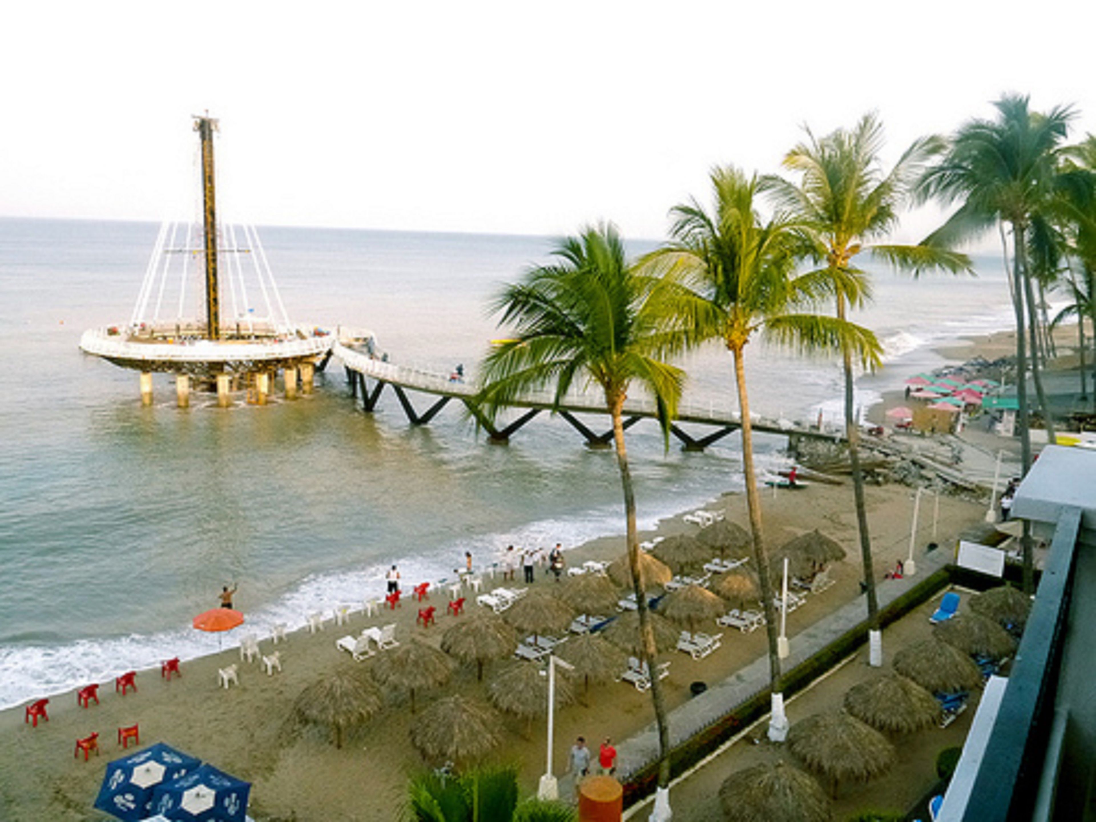 A beach with a pier, palm trees, and beach chairs.