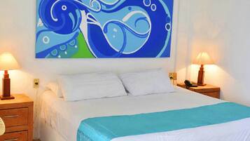 A hotel room with a large bed, white bedding, a blue and white abstract painting on the wall, and two bedside lamps.