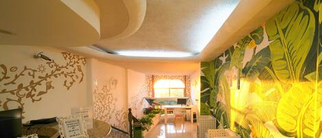 A hotel lobby with a reception desk, a computer, a window, and a wall with a tropical mural.
