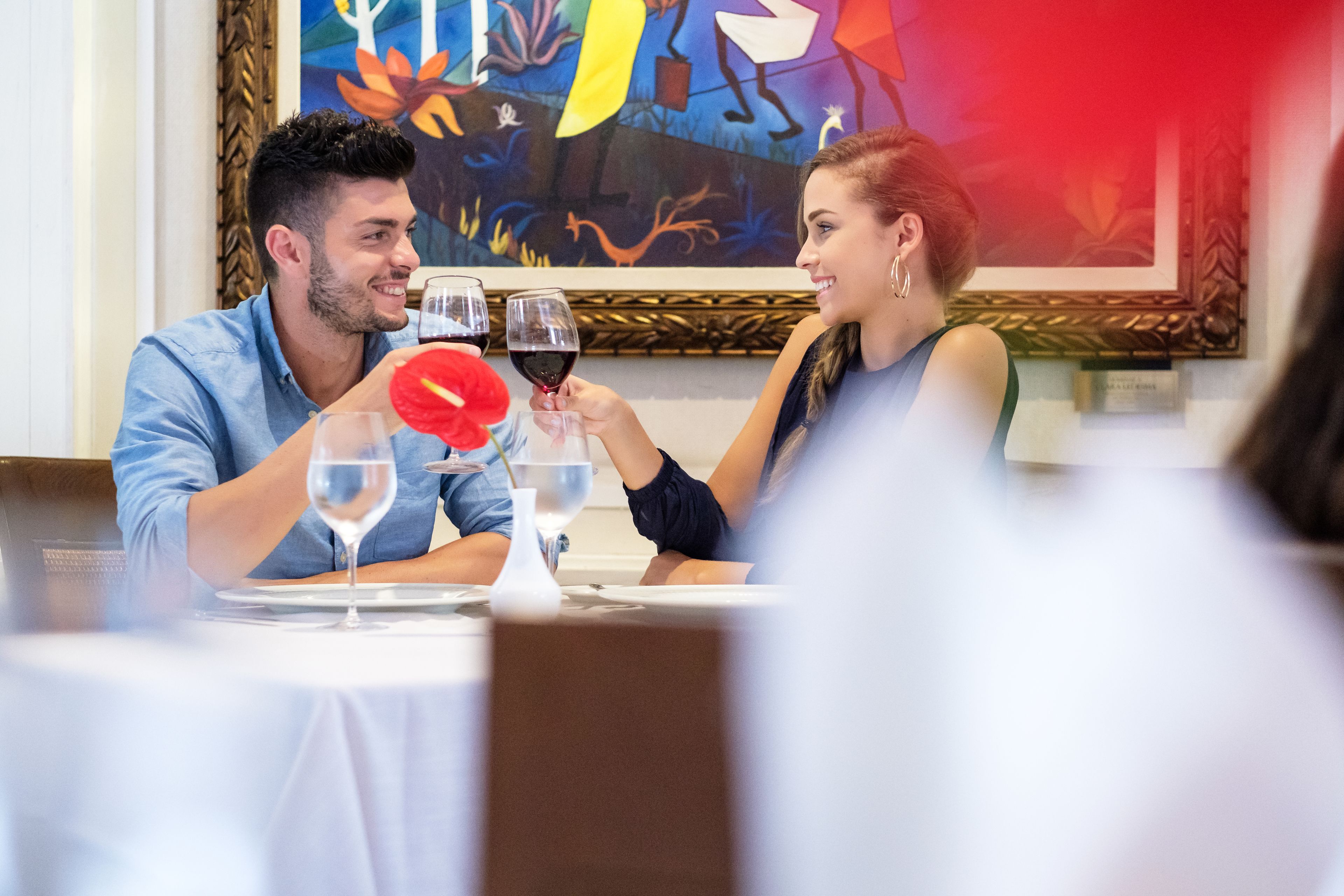 A dining table with two people toasting with wine glasses.
