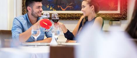 A dining table with two people toasting with wine glasses.