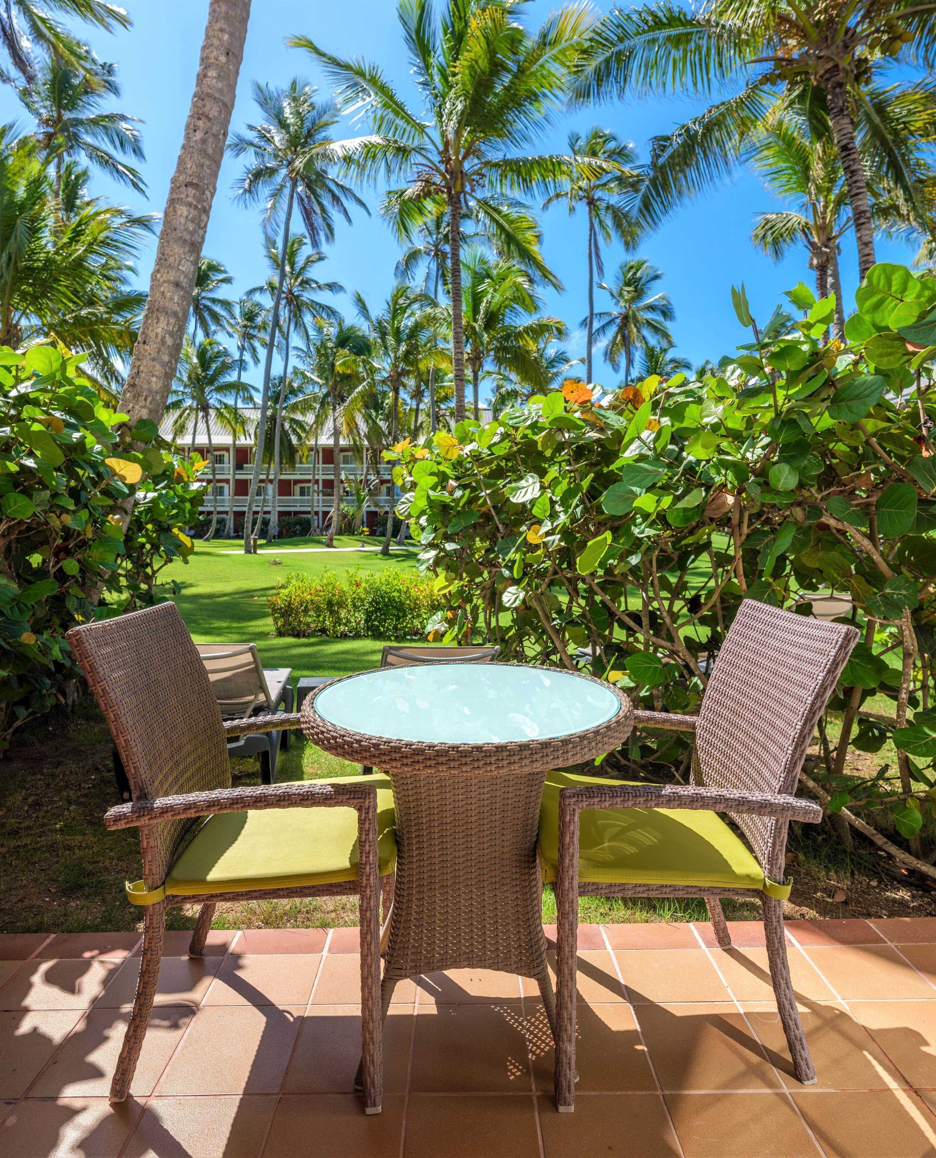 A wicker table with two chairs, a green cushion, and a view of a golf course and palm trees.