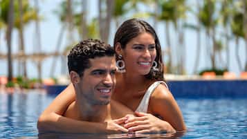A couple in a swimming pool with a tropical background.